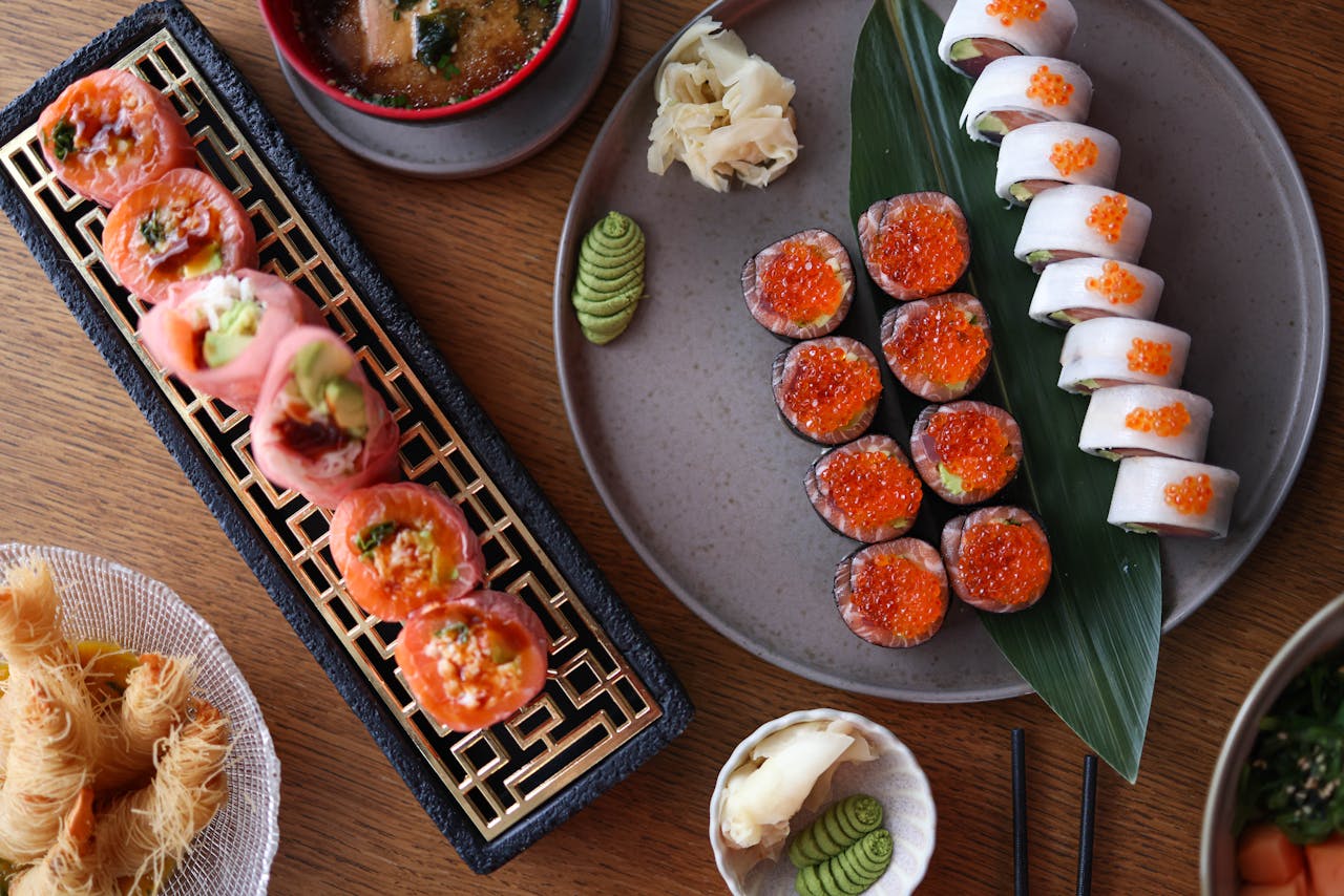 services-03 Top-down view of an assorted sushi platter with wasabi, ginger, and dipping sauces on a wooden table.